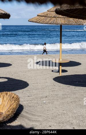 Die Menschen flüchten zwischen den unbenutzten Sonnenschirmen, die während der ersten Phase der Deeskalation des Covid 1 am Strand von Playa Fanabe Sport treiben Stockfoto