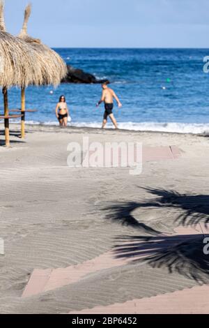 Die Menschen flüchten zwischen den unbenutzten Sonnenschirmen, die während der ersten Phase der Deeskalation des Covid 1 am Strand von Playa Fanabe Sport treiben Stockfoto