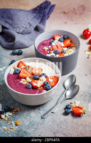 Zwei farbige Beeren Smoothie Schüssel mit Müsli, Heidelbeere und Kokosnuss, grauer Hintergrund. Gesundes veganes Food-Konzept. Stockfoto