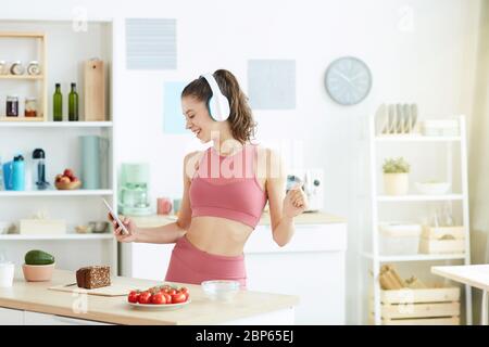 Taille-up-Porträt von lächelnden jungen Frau tanzen in der Küche und hören Musik während der Vorbereitung Fitness-Mittagessen, kopieren Raum Stockfoto