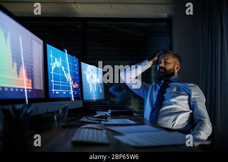 Frustrierter Geschäftsmann mit Computer an der Rezeption, der spät arbeitete. Konzept der Finanzkrise. Stockfoto