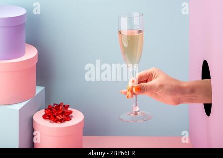 Weibliche Hand hält ein Glas Sekt auf blauem und rosa Hintergrund Stockfoto