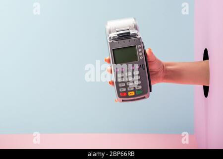 Hand hält ein POS-Terminal mit gedrucktem Beleg auf blauem und rosa Hintergrund Stockfoto