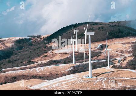 Elektrische Turbine Windmühle auf einem verschneiten Boden. Winterhügellandschaft mit blauem Himmel. Stockfoto