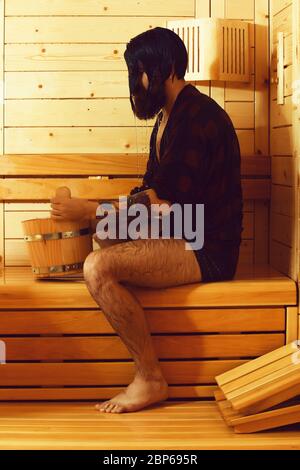 Schöner Mann oder Badende, bärtigen Hipster mit Bart und Schnurrbart in rot kariertem Hemd von der Schaufel gießt Wasser auf dem Kopf in der Sauna, Thermalbad auf hölzernen Hintergrund Stockfoto