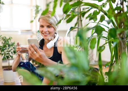 Vorderansicht der jungen Sportlerin mit Smartphone im Innenbereich zu Hause, ausruhen. Stockfoto