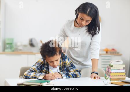 Porträt der jungen afrikanischen Mutter helfen Teenager-Jungen zu Hause studieren in minimalen weißen Innenraum, kopieren Raum Stockfoto