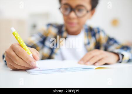 Nahaufnahme von niedlichen afrikanischen Jungen Schreiben in Notizbuch während Hausaufgaben, Fokus auf Vordergrund, kopieren Raum Stockfoto