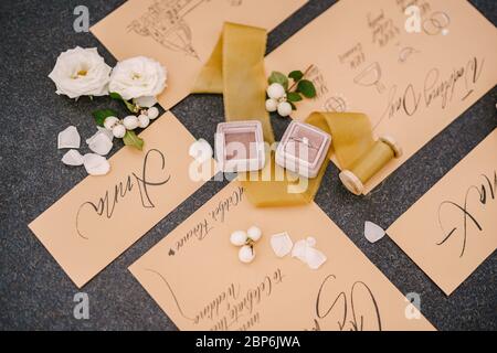 Eheringe in einer Schachtel, Einladungskarten, Seidenband, weiße Rosen auf schwarzem Hintergrund. Ansicht von oben. Stockfoto