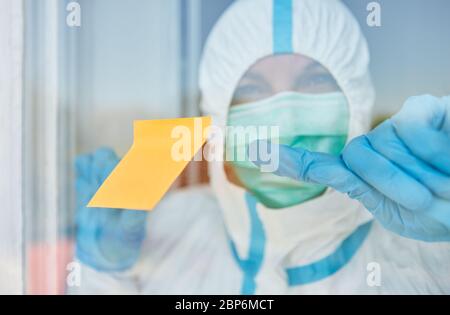 Gelbe Haftnotiz schlüpfen an Tür oder Fenster der Klinik mit Arzt in Schutzkleidung während der Coronavirus-Epidemie Stockfoto