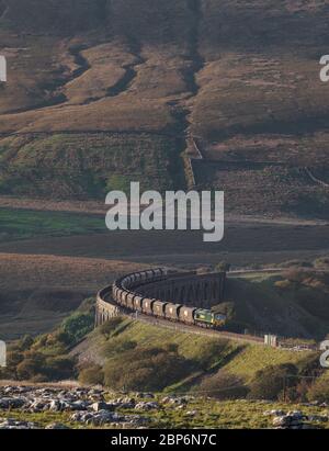 Freightliner 66 Lok 66510 läuft mit einem fröhlichen Kohlebad-Zug vom Ribblehead-Viadukt ab, über dem sich die Landschaft erhebt Stockfoto