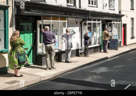 Eine Schlange, die eine sichere soziale Distanz außerhalb der lokalen Apotheke in der kleinen walisischen Stadt Presteigne, Powys, Wales, Großbritannien, aufrecht erhält Stockfoto