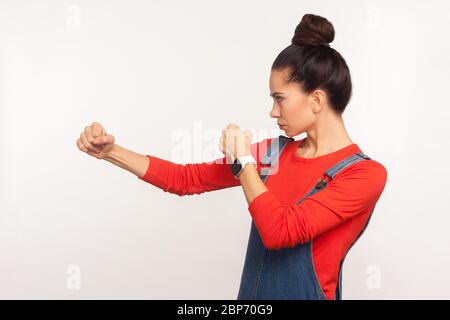 Lasst uns kämpfen! Seitenansicht von entschlossenen selbstbewussten Mädchen mit Haar-Bun in Denim Overalls Stanzen, Boxen mit geballten Fäusten, Kampf und Selbstverteidigung. ich Stockfoto