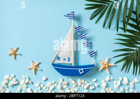 Nautische Komposition mit Segelboot, Palmenblättern und Seesternen auf blauem Hintergrund. Sommerurlaub und Tourismus-Wohnung lag mit Meer Reiseobjekt Stockfoto