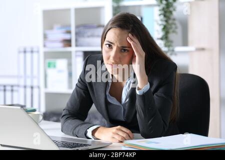Traurige Exekutive Frau, die sich die Kamera im Büro auf ihrem Schreibtisch ansieht Stockfoto