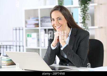 Glückliche Exekutive Frau posiert auf Kamera sitzen auf einem Schreibtisch im Büro Stockfoto