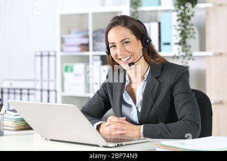 Glückliche Telemarketerin Frau mit Headset und Laptop posiert Blick auf Kamera sitzt auf einem Schreibtisch im Büro Stockfoto