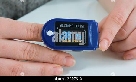 Frau, die in ihren Händen blaues Pulsoximeter hält. Monitor zeigt die Sauerstoffsättigung im Blut und die Pulsfrequenz des Patienten an. Nahaufnahme. Stockfoto