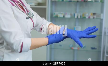 Junge kaukasische Nurce in weißen medizinischen Mantel und violetten Stethoskop suchen und überprüfen Sie einen Gummi-blauen Handschuhe, wenn es undicht ist und verwendet werden kann. Seitenansicht Stockfoto