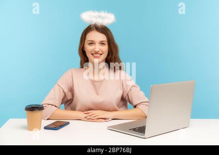 Schöne Engel glücklich Frau Angestellter mit Nimbus sitzt am Arbeitsplatz und Blick auf die Kamera mit toothy Lächeln, freundliche freundliche Sekretärin an der Rezeption. In Stockfoto