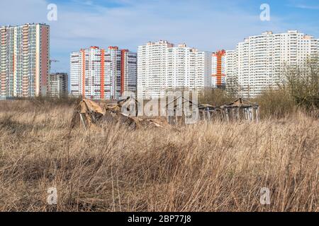 Auf einem alten verlassenen Feld befindet sich ein zerstörtes Gewächshaus für Gemüse vor dem Hintergrund von mehrstöckigen Gebäuden im Bau Stockfoto