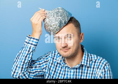 Mann setzt auf einen Hut aus Aluminiumfolie mit erfreut Gesicht.. Schützt vor dem Lesen denken. Stockfoto