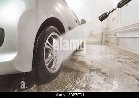 Selbstreinigende stilvolle Auto in der Garage. Waschen kolesnogo fahren. Reinigung Auto mit hohem Druck Wasser. Mann sein Auto waschen unter hohem Druck Wasser Stockfoto