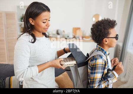 Seitenansicht Porträt von lächelnden afroamerikanischen Frau, die Bücher in Rucksack während der Sendung Sohn zur Schule Stockfoto