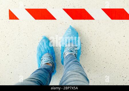 Frau stehen in der Linie halten soziale Distanz tragen Überschuhe, medizinische Schuhüberzüge im Krankenhaus.Draufsicht Mann hinter einer Warnlinie während Stockfoto