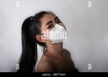 Nahaufnahme der jungen Asienfrau, die eine medizinische Maske n95 aufsetzt, um vor Atemwegserkrankungen wie der Grippe-covid-19 PM2.5 Staub und Smog bei gr Stockfoto