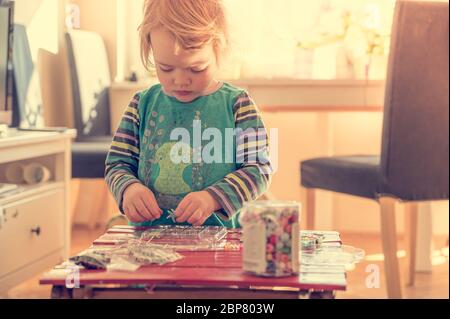 Cute blonde Mädchen spielen mit vielen bunten Perlen zu Hause. Stockfoto