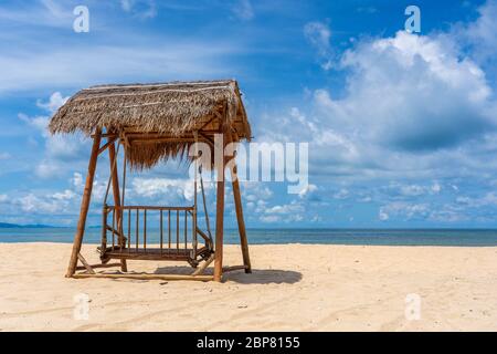 Holzschaukel unter einem Strohdach an einem tropischen Sandstrand in der Nähe des Meeres auf der Insel Phu Quoc, Vietnam. Reise- und Naturkonzept Stockfoto