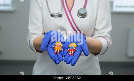 Kaukasische junge Frauen Medic in Gummi-blauen Handschuhen hält Spielzeugfiguren von Kinderund nah an ihrem Herzen auf einem weißen Hintergrund. Mittlere Aufnahme. Kinder pro Stockfoto