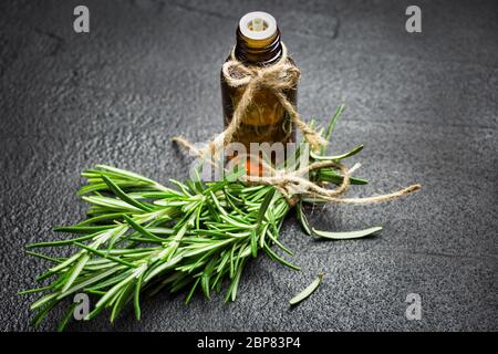 Rosmarin Kräuterzweige und Flasche Rosmarin ätherisches Öl auf schwarzem Stein Hintergrund. Kräuteraromatherapie Konzept. Stockfoto