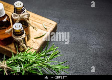 Rosmarin Kräuterzweige und Flaschen Rosmarin ätherisches Öl auf schwarzem Stein Hintergrund. Kräuteraromatherapie Konzept. Stockfoto