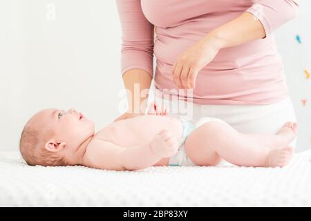 Mutter steht neben dem Bett mit ihrem Neugeborenen baby boy liegend auf seinem Rücken. Baby Boy auf einem Bett trug eine Windel an der Mutter und lächelnd. Stockfoto