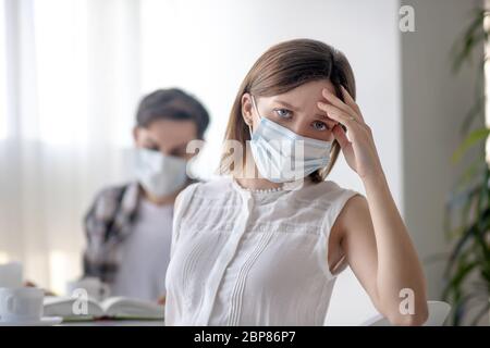 Junge Frau in einer Gesichtsmaske mit Kopfschmerzen Stockfoto