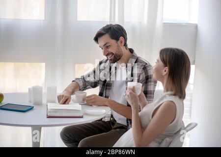 Dunkelhaariger Mann und seine schwangere Frau sitzen in der Küche und fühlen sich gut Stockfoto