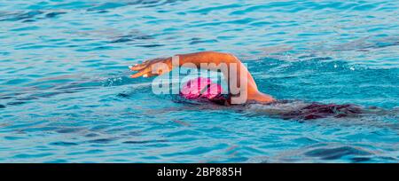 Horizontale Ansicht einer Schwimmerin, die mit einem Freestyle-Schlaganfall in einem Freibad schwimmt, das für einen Triathlon trainiert. Stockfoto