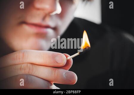 Der Mann hält ein dünnes Holzkitzelholz in der Hand, das in der Dunkelheit mit einer hellen warmen Flamme brennt. Stockfoto