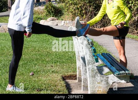 Zwei Läufer strecken ihre Oberschenkel mit einer Parkbank, bevor sie laufen. Stockfoto