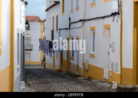 Gepflasterte Gasse zwischen weiß getünchten Hauswänden mit Farbakzenten und Wäsche, die in der traditionellen Nachbarschaft an den Linien trocknen kann Stockfoto