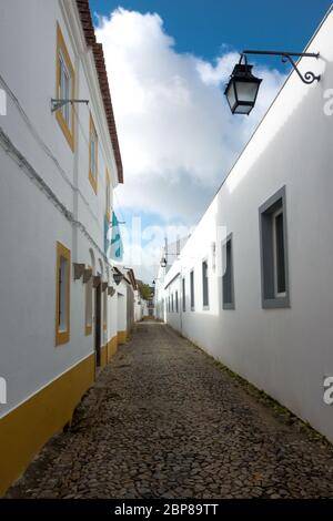 Gepflasterte Gasse zwischen weiß getünchten Hauswänden mit Farbakzenten in einem traditionellen Viertel in der historischen Altstadt von Evora in Port Stockfoto