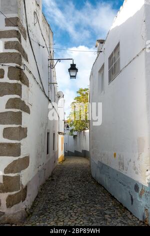 Gepflasterte Gasse zwischen weiß getünchten Hauswänden mit Farbakzenten in einem traditionellen Viertel in der historischen Altstadt von Evora in Port Stockfoto