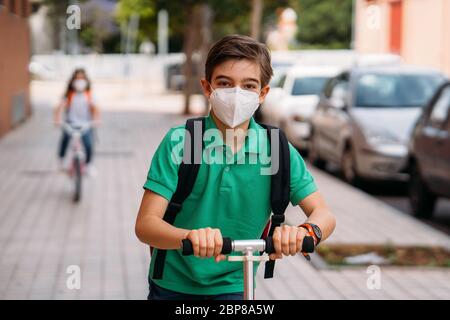 Junge und Mädchen tragen Masken und fahren einen Roller und Fahrrad auf der Straße Stockfoto