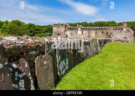 Verwitterte Grabsteine an der Außenmauer zur Saint David's Cathedral mit dem Bischofspalast im Hintergrund, Pembrokeshire, Wales Stockfoto