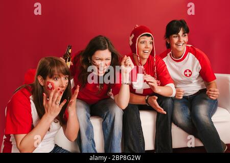 Foto von weiblichen Schweizer Sport-Fans vor dem Fernseher und ihr Team anfeuern. Stockfoto