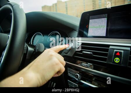 Weibliche Finger drückt Start-Stopp-Motor-Taste auf einem Auto Armaturenbrett. Close-up, Soft-Fokus, im Hintergrund Auto Innenraum Details in Unschärfe, Seitenansicht Stockfoto