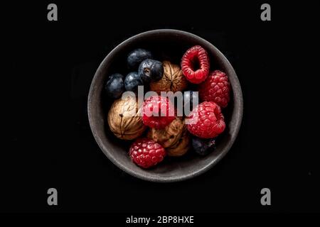 Brombeeren und Walnüsse in einer kleinen grauen Schüssel mit schwarzem Hintergrund der High-Key-Studie. Stockfoto