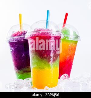 Stillleben Nahaufnahme von bunten Regenbogen geschichteten gefrorenen Früchten Slush Getränke auf Eis bedeckt weiße Oberfläche in Kunststoff Take Away Tassen mit Drinkin angeordnet Stockfoto